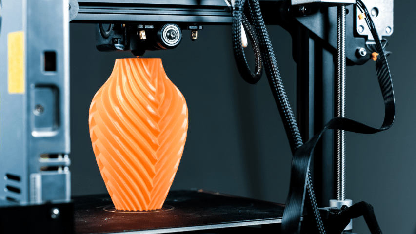 3D printer creating an orange vase with swirling lines.