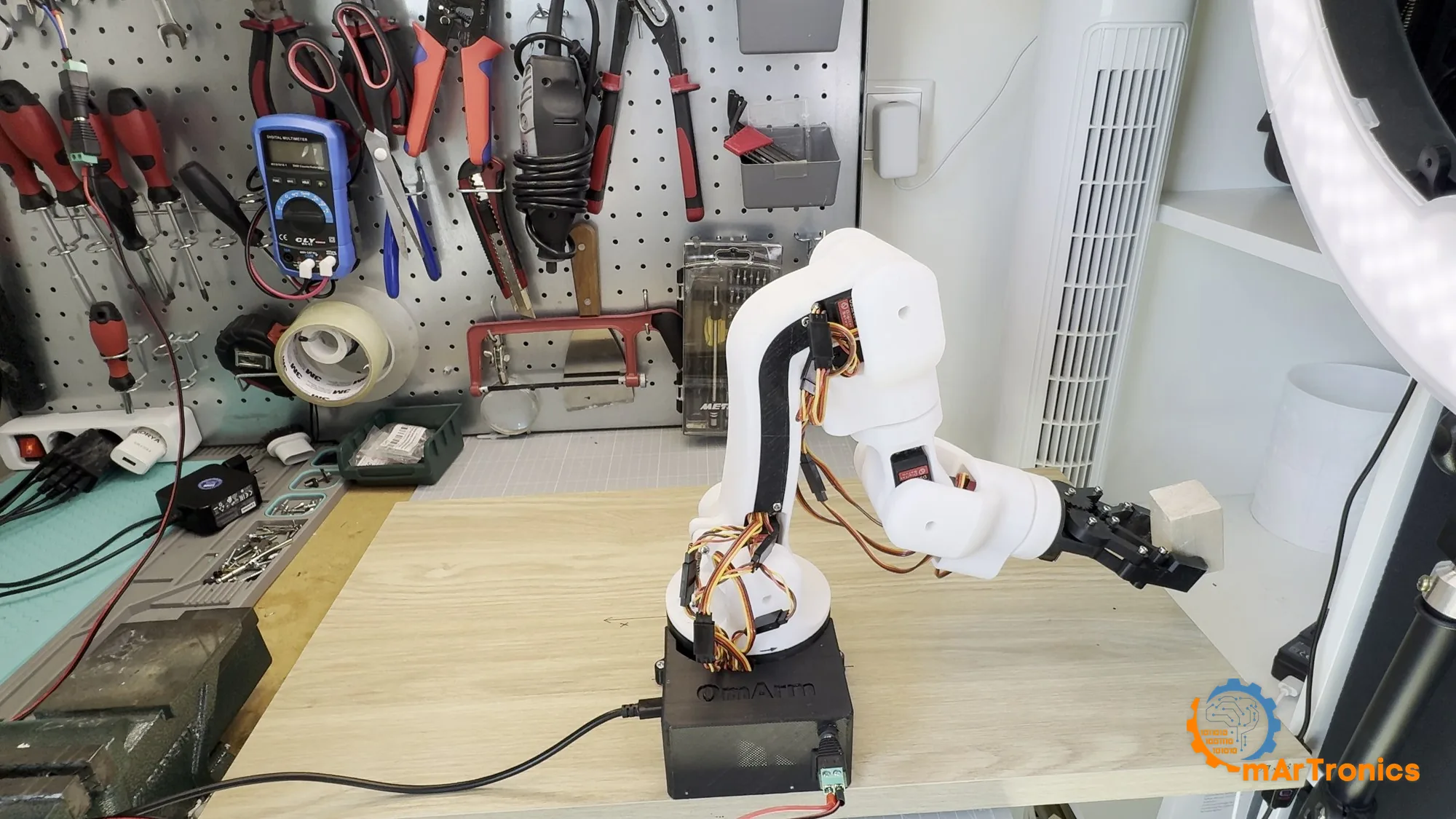 The assembled OmArm One standing on the workbench with its gripper out over a wooden block
